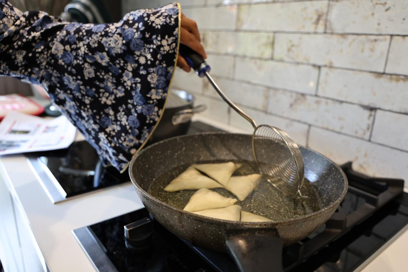 Lady reaching over a pan of hot oil with kitchen utensils. Her long sleeves are dangerously close to the pan.